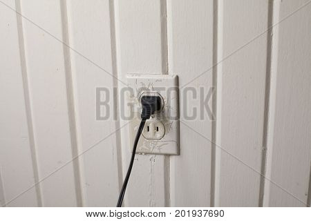 Black cord plugged into an outlet on an off-white wall