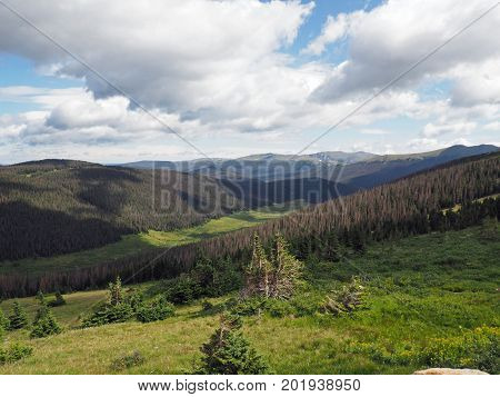 Summer in the Rocky Mountains National Park in Colorado. White puffy clouds in a blue sky cast shadows over the moutains and meadows below