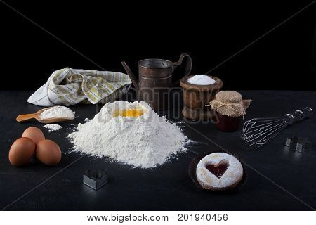 Pastry cookie with a red jam heart and icing powder sugar and cooking utensils on table