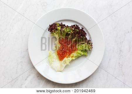 Top view of red caviar on a salad leaf on a light marble background. copy space, Top view.