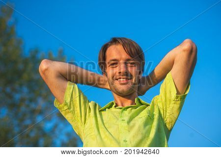 A color portrait photo of a happy smiling brunette haired man wearing a yellow lime green shirt against a blue sky backround.