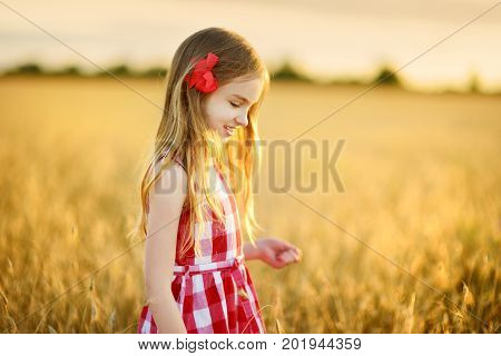 Adorable Girl Walking Happily In Wheat Field On Warm And Sunny Summer Evening