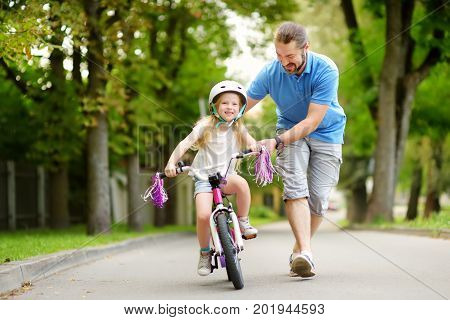 Happy Father Teaching His Little Daughter To Ride A Bicycle. Child Learning To Ride A Bike.