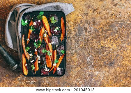Baked beets and carrots in a vintage black pan with ricotta fennel seeds and fresh coriander leaves on a rusty background autumn dish. Top view.
