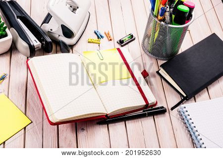 Top view workspace mockup on wooden background with blank notebook with copy space, pen, tacker, punch, clips and accessories. Overhead view. Flat lay, top view