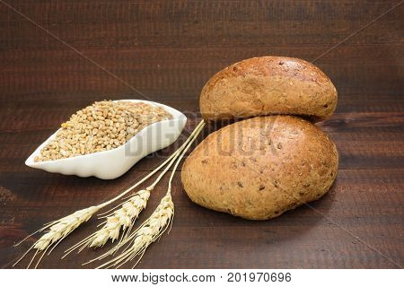 Bread, grains of wheat and spikes on brown wooden background