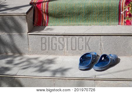 Blue sliders on steps of a house with open door, curtain lace and green-red footcloth