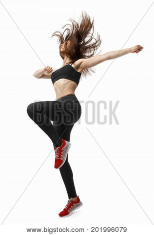 Beautiful young fit modern dancer lady in black sportswear warming up, working out, dancing with her long hair flying, full length, studio image on isolated white background.