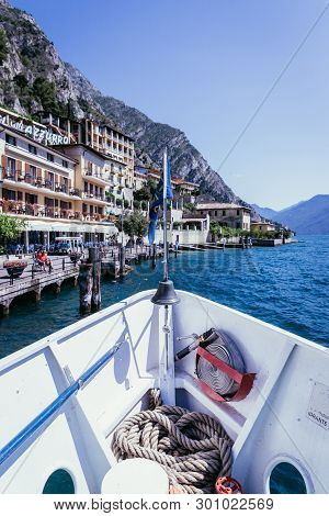Bow Of A Boat On A Boat Tour. Blue Water, Moutnain Range And Little Village, Lago Di Garda, Italy