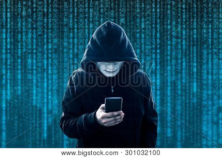Hooded hacker with mask holding smartphone 