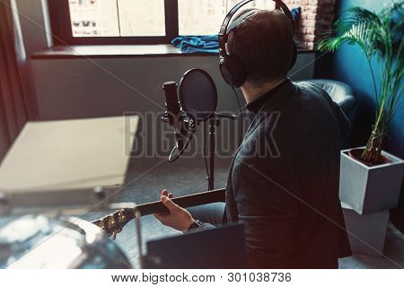 Close Up Of A Man Singer Sitting On A Stool In A Headphones With A Guitar Recording A Track In A Hom
