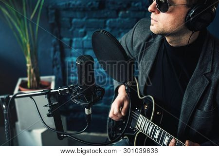 Close Up Of A Man Singer Sitting On A Stool In A Headphones With A Guitar Recording A Track In A Hom