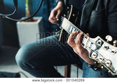 Close Up Of A Man Singer Sitting On A Stool In A Headphones With A Guitar Recording A Track In A Hom
