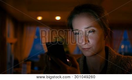 Woman Using Smartphone In Cafe Of Cruise Ship. Evening Time, Lowlight. Technology And Entertainment 