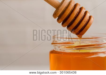 A Viscous Stream Of Sweet Amber Flower Honey Flows From A Wooden Honey Spoon Into A Glass Jar.