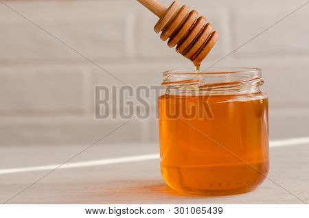 A Viscous Stream Of Sweet Amber Flower Honey Flows From A Wooden Honey Spoon Into A Glass Jar.