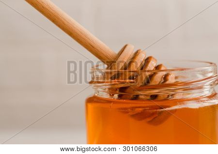 A Wooden Honey Spoon Is Immersed In A Glass Jar Filled With Fresh Floral Honey.