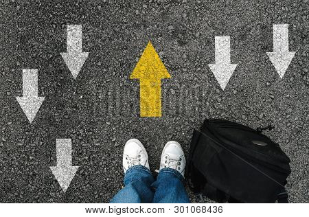 Man Shoes And Backpack On Asphalt And Opposing Direction Arrows On Asphalt Ground, Personal Perspect