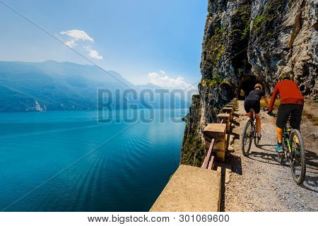 Cycling woman and man riding on bikes at sunrise mountains and Garda lake landscape. Couple cycling MTB enduro flow sentiero ponale trail track. Outdoor sport activity.