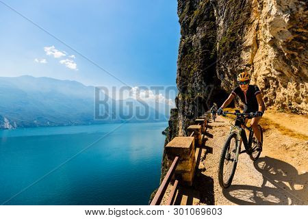 Cycling woman and man riding on bikes at sunrise mountains and Garda lake landscape. Couple cycling MTB enduro flow sentiero ponale trail track. Outdoor sport activity.