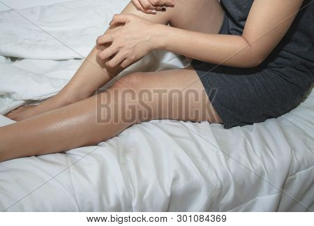 Asian Girl Wearing Gray Dress Itching In The Legs. The Woman Was Scratching Her Leg.in A White Bedro