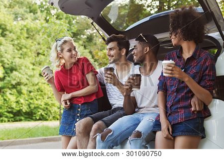 Happy Multicultural Couples Sitting In Open Car Back, Having Stopover, Drinking Coffee.