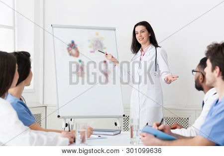 Medical Lecture. Woman Telling Theory To Interns Using Whiteboard And Pictures