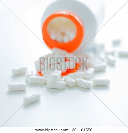 White Tablets Spilling Out Of A Plastic White Bottle With A Tablet