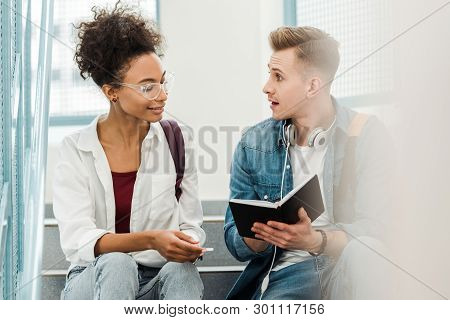 Two Multiethinc Students With Notebook Sitting On Stairs In University