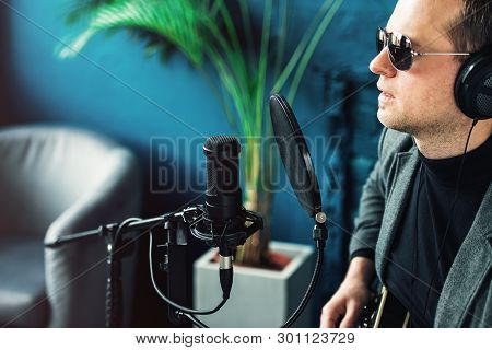 Close Up Of A Man Singer Sitting On A Stool In A Headphones With A Guitar Recording A Track In A Hom