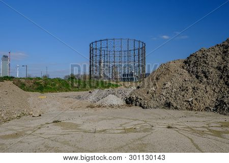 Pile Of Earth With A Concrete Base In The Foreground And An Old Gasworks In The Background.  Site Be