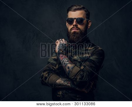 Bearded Tattooed Guy In Military Shirt And Sunglasses Posing With Thoughtful Look. Studio Photo Agai