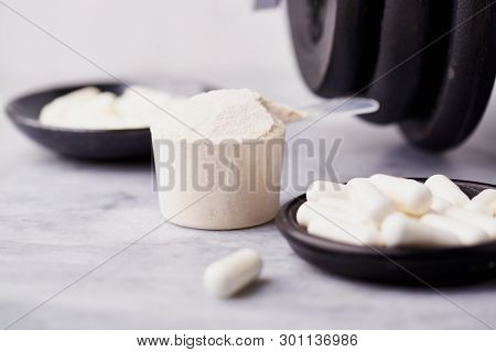 Scoop Of Whey Protein, Creatine, Taurine Capsules And A Dumbbell. Bodybuilding Food Supplements On S