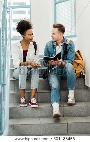Two Multiethinc Students With Notebook Sitting On Stairs In University