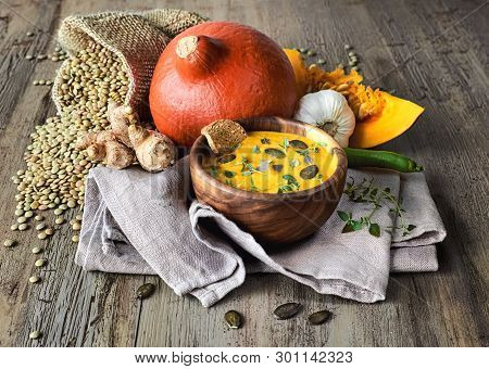 Spicy Pumpkin And Lentil Creme Soup Served In Olive Wood Bowl With Thyme Leaves, Pumpkin Seeds And C