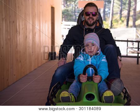 Excited young father and son driving on alpine coaster while enjoying beautiful sunny day in the nature