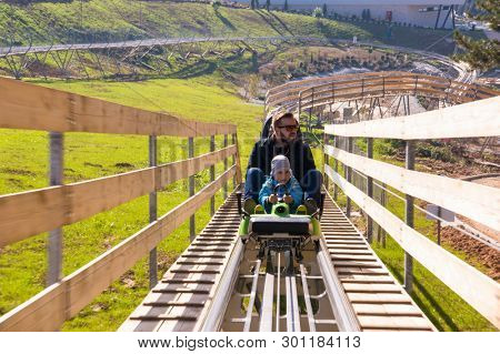 Excited young father and son driving on alpine coaster while enjoying beautiful sunny day in the nature
