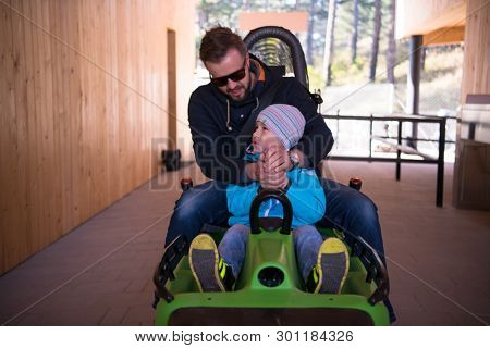 Excited young father and son driving on alpine coaster while enjoying beautiful sunny day in the nature