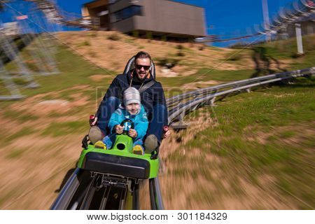 Excited young father and son driving on alpine coaster while enjoying beautiful sunny day in the nature