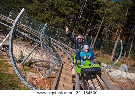 Excited young father and son driving on alpine coaster while enjoying beautiful sunny day in the nature