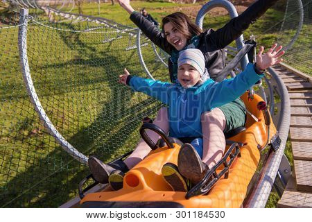 Excited young mother and son driving on alpine coaster while enjoying beautiful sunny day in the nature