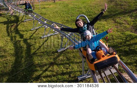 Excited young mother and son driving on alpine coaster while enjoying beautiful sunny day in the nature