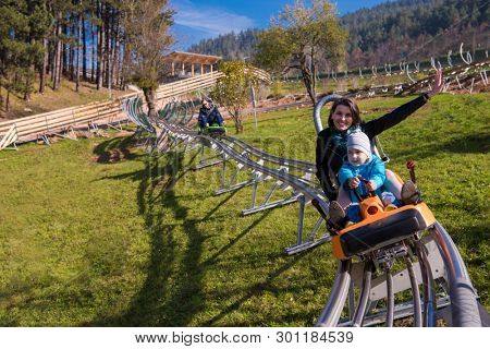 Excited young mother and son driving on alpine coaster while enjoying beautiful sunny day in the nature