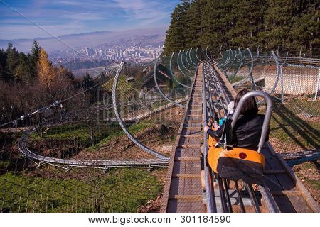 Excited young mother and son driving on alpine coaster while enjoying beautiful sunny day in the nature