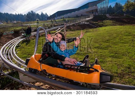 Excited young mother and son driving on alpine coaster while enjoying beautiful sunny day in the nature