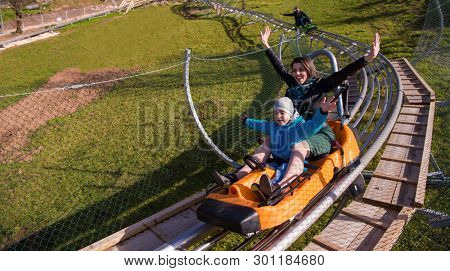 Excited young mother and son driving on alpine coaster while enjoying beautiful sunny day in the nature