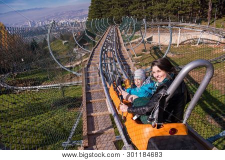 Excited young mother and son driving on alpine coaster while enjoying beautiful sunny day in the nature