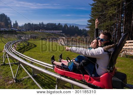 Excited young couple driving alpine coaster while enjoying beautiful sunny day in the nature