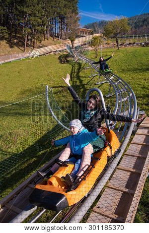 Excited young mother and son driving on alpine coaster while enjoying beautiful sunny day in the nature
