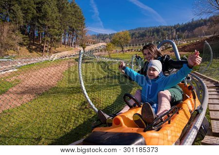 Excited young mother and son driving on alpine coaster while enjoying beautiful sunny day in the nature
